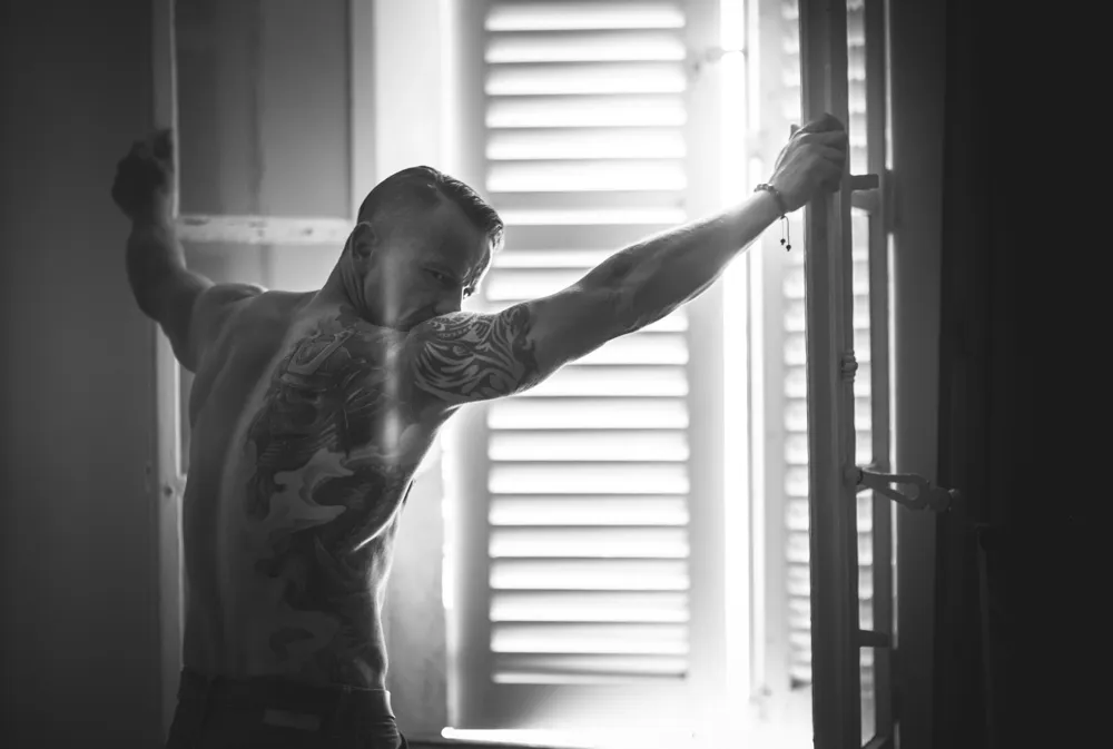 Portrait d'un homme tatoué torse nu se tenant à une fenêtre lors d'un shooting photo à Draguignan